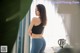 A woman in a black top and blue jeans standing by a window.