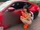 A woman in an orange outfit posing next to a red car.