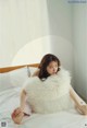 A woman sitting on a bed holding a fluffy white pillow.