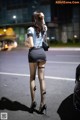 A woman in fishnet stockings and high heels standing next to a car.